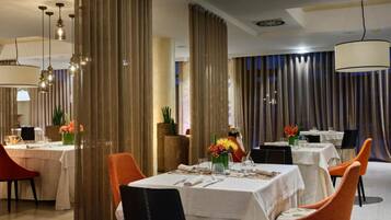 A dining area with tables set for two, featuring white tablecloths and orange chairs.