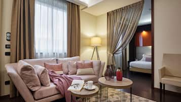 Moderni hotellihuone, jossa on sohva, pieni pyöreä pöytä, lamppu ja sänky.