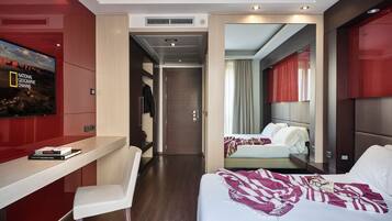 A modern hotel room with a desk, a bed, and a television displaying the National Geographic Channel.