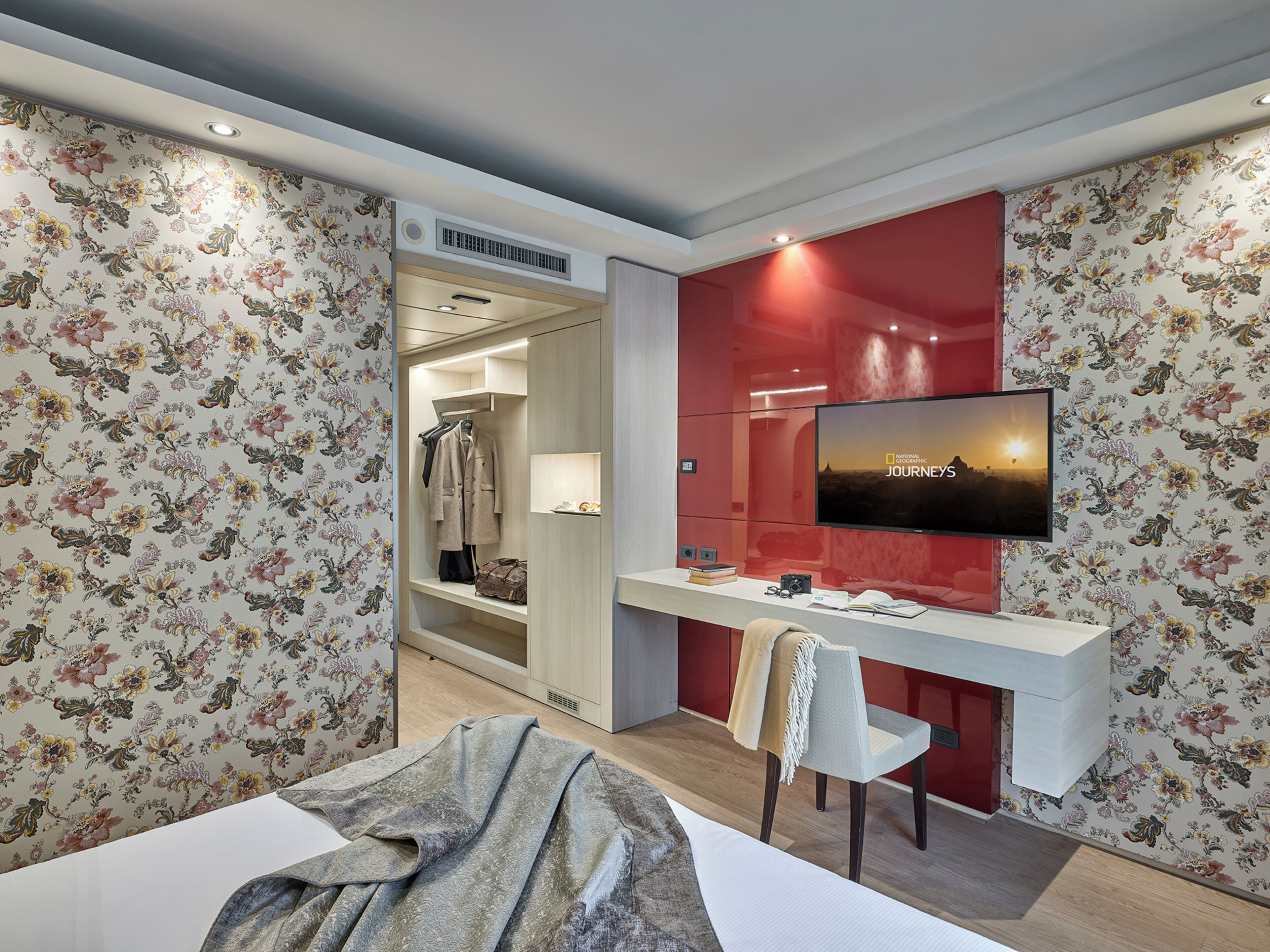Ein Hotelzimmer mit einem Bett, einem Schreibtisch mit Stuhl, einem an der Wand montierten Fernseher und einem Kleiderschrank.