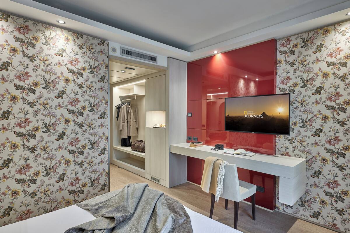 Ein Hotelzimmer mit einem Bett, einem Schreibtisch mit Stuhl, einem an der Wand montierten Fernseher und einem Kleiderschrank.