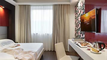 A hotel room with a bed, a desk with a chair, a television, and a window with curtains.