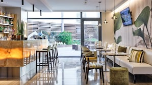 Un moderno vestíbulo de hotel con zona de bar, asientos y un amplio ventanal con vistas al exterior.