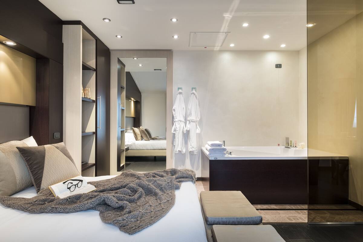 Ein modernes Hotelzimmer mit einem großen Bett, einer Sitzecke, einem separaten Badezimmer mit Badewanne und einem begehbaren Kleiderschrank.