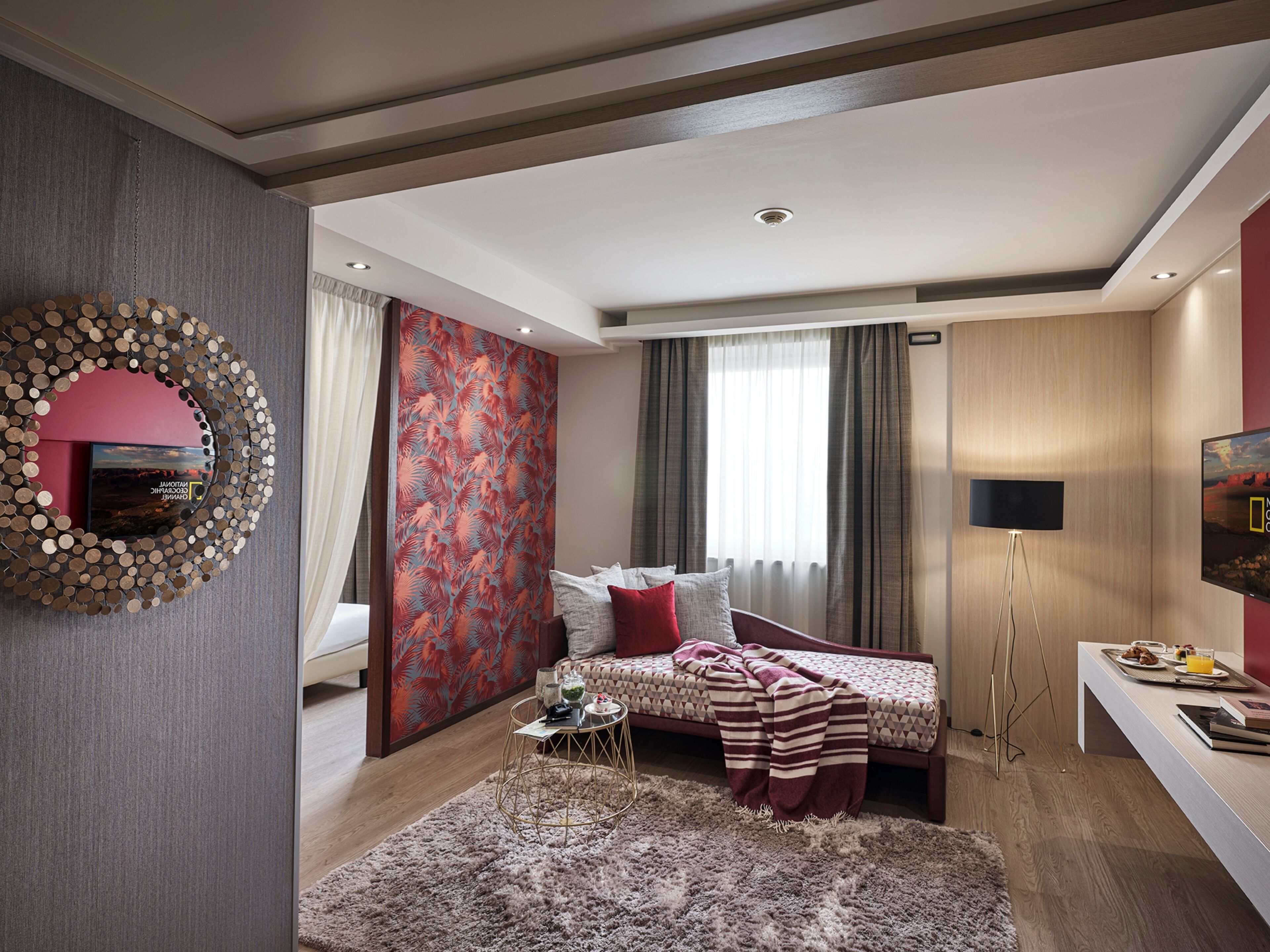 A modern bedroom with a bed, a round mirror, a TV, and a desk with breakfast items.