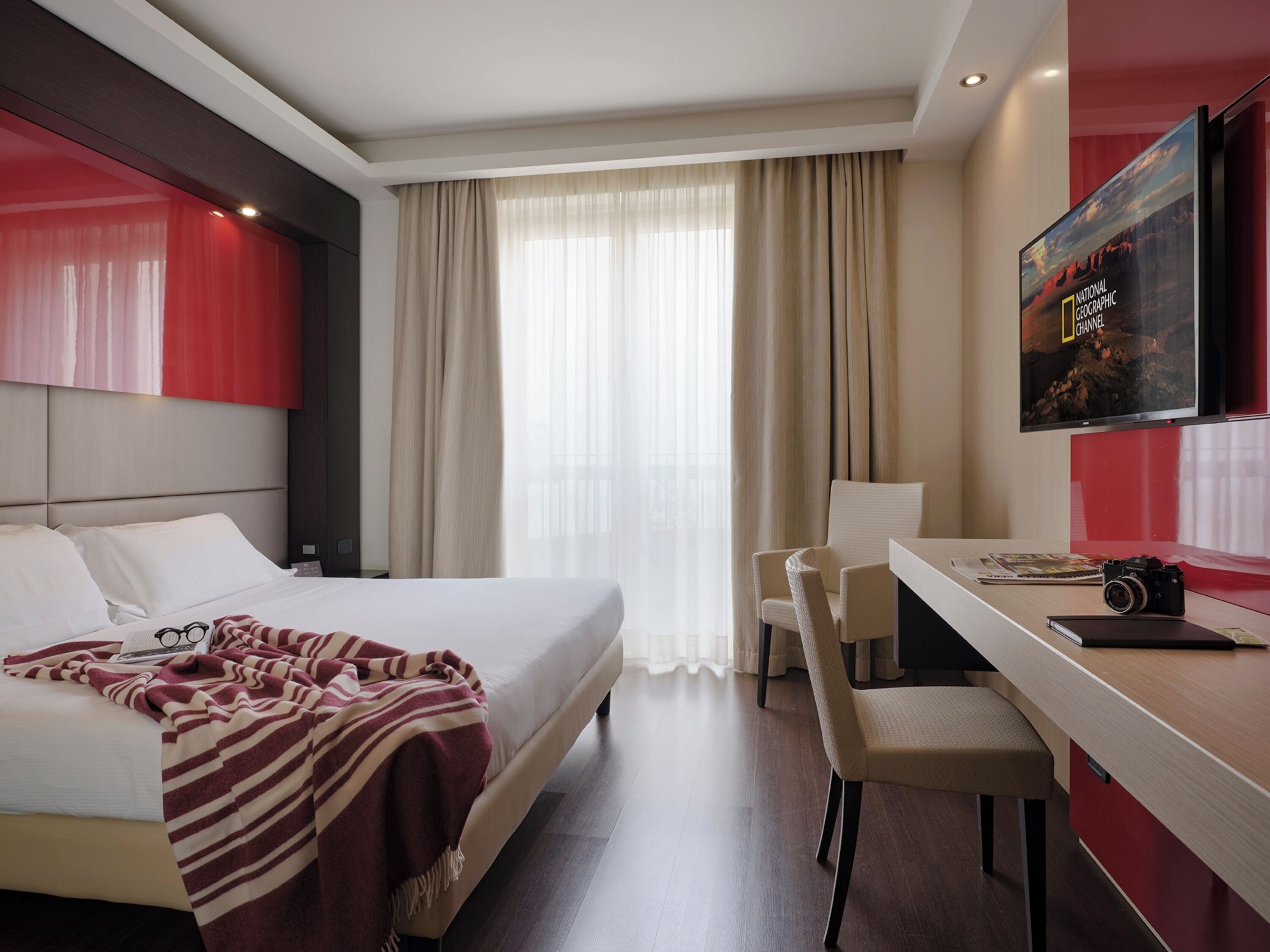 A hotel room with a bed, a desk, a chair, a television, and a window with curtains.