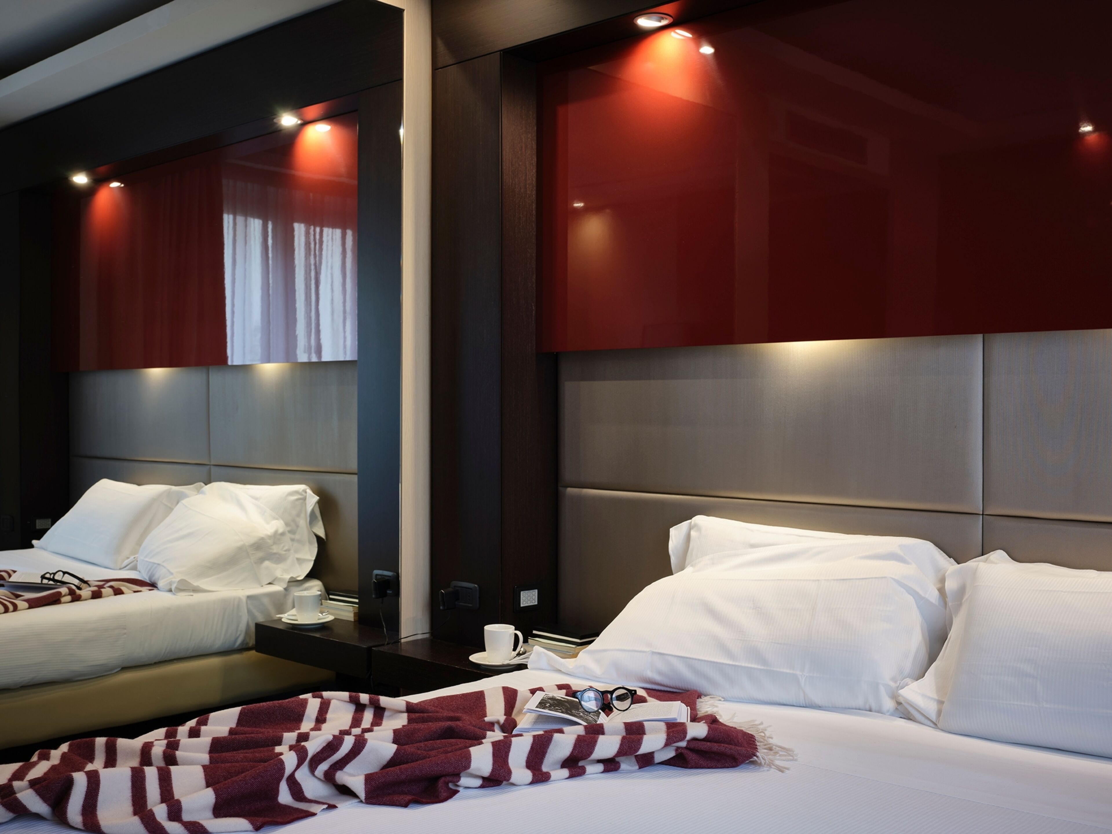 A hotel room with a large bed, a bedside table, a mirror, and a red-striped blanket.