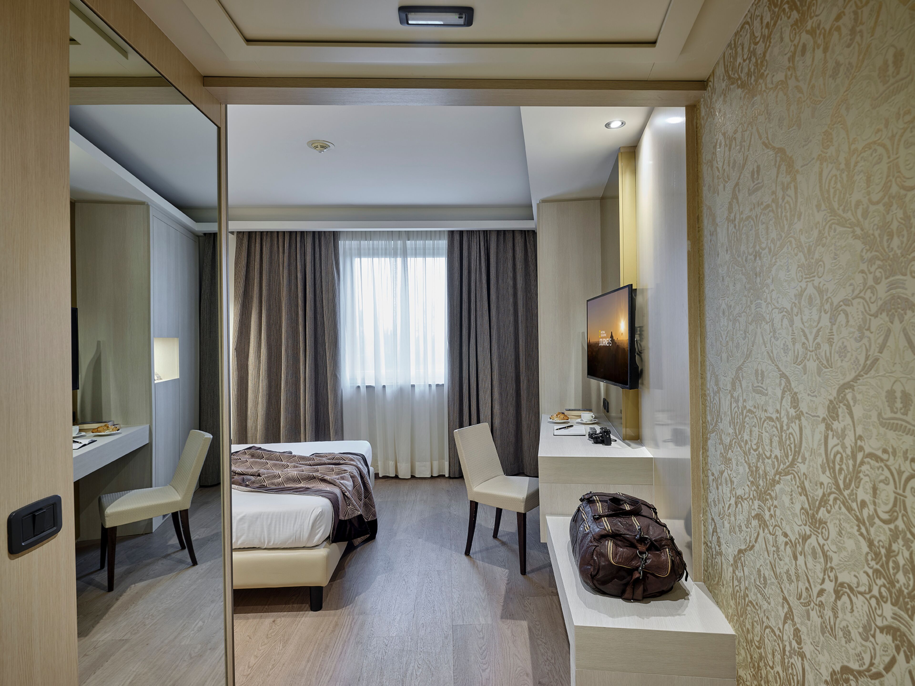 Una habitación de hotel con una cama, un escritorio con computadora, una silla y un espejo grande.