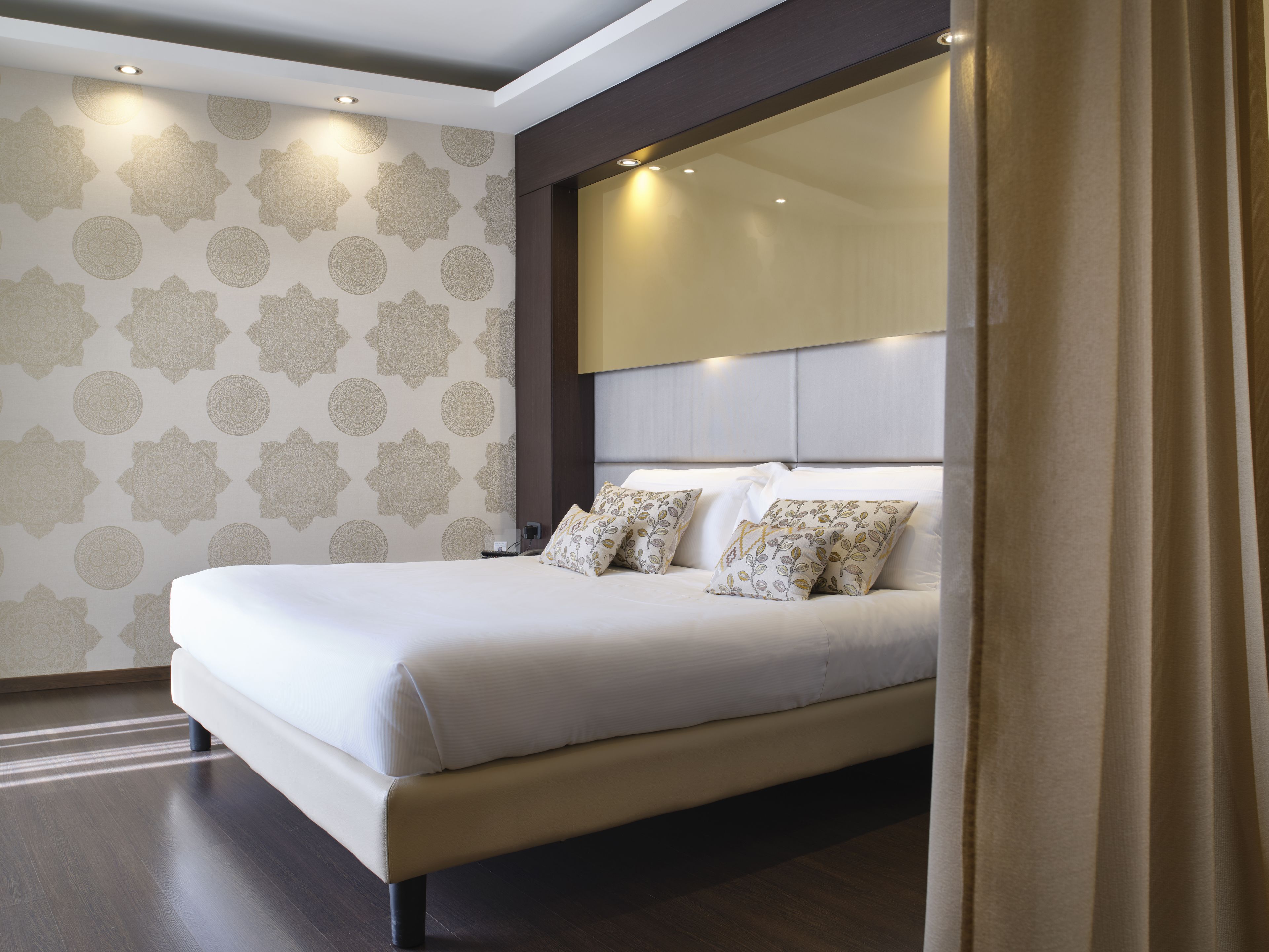 A modern bedroom with a large bed, a headboard with integrated lighting, and patterned wallpaper.