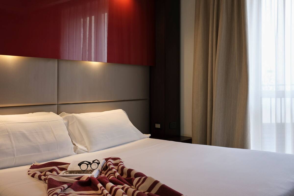 Ein Hotelzimmer mit einem großen Bett, einer roten Akzentwand und einem Fenster mit Vorhängen.