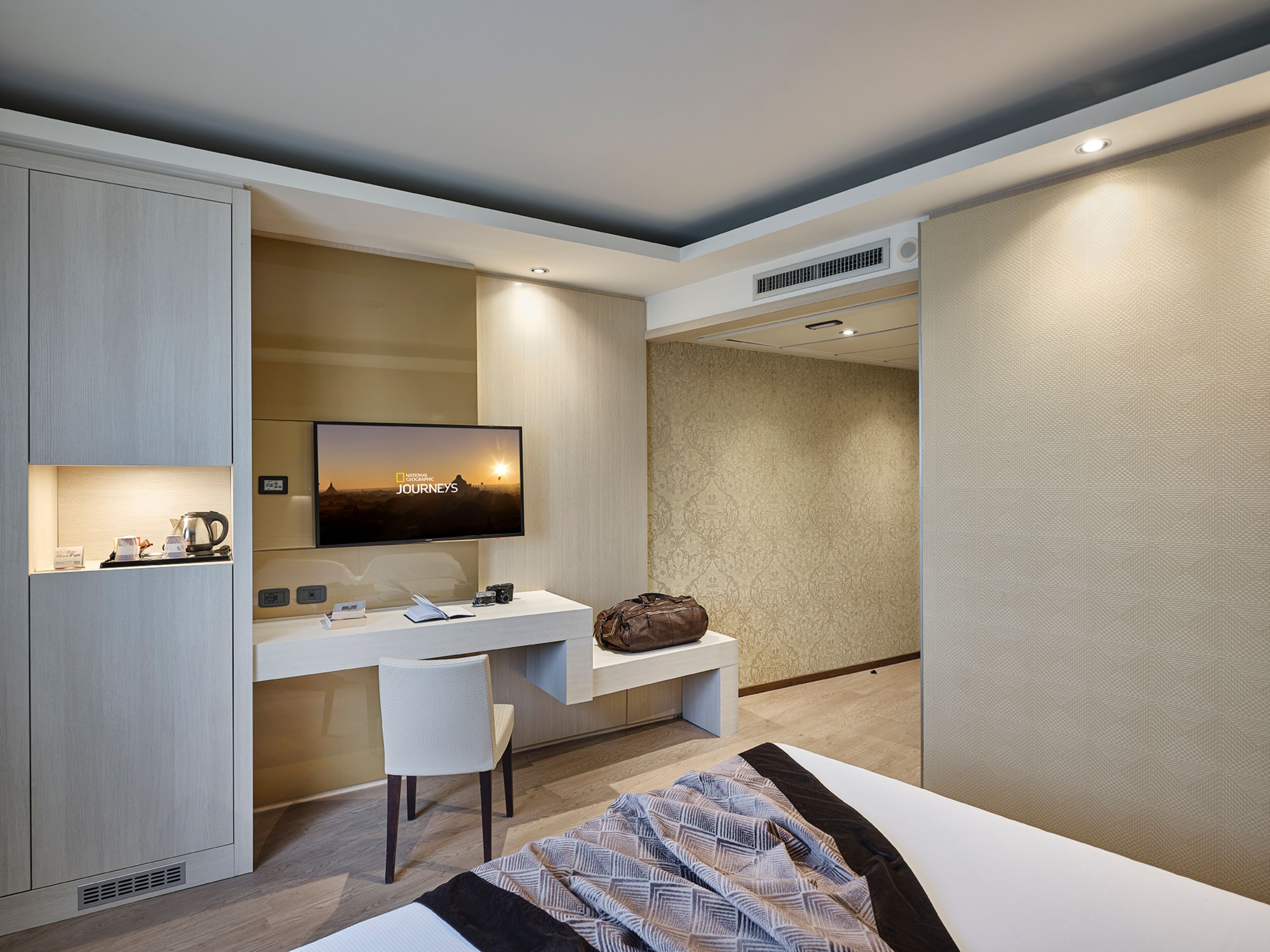 Una habitación de hotel moderna con cama, escritorio, silla, televisor y armario.