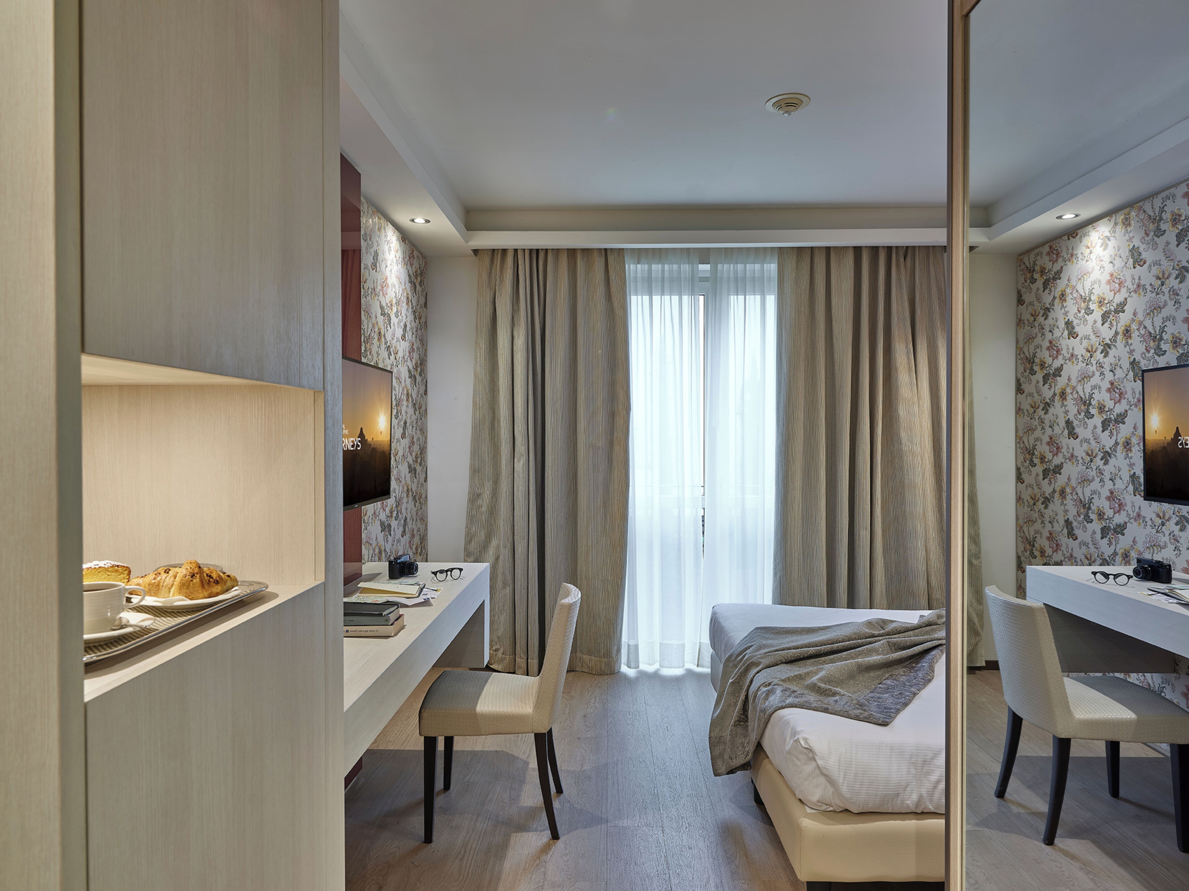 A hotel room with a bed, a desk, a chair, a television, and a large window with curtains.