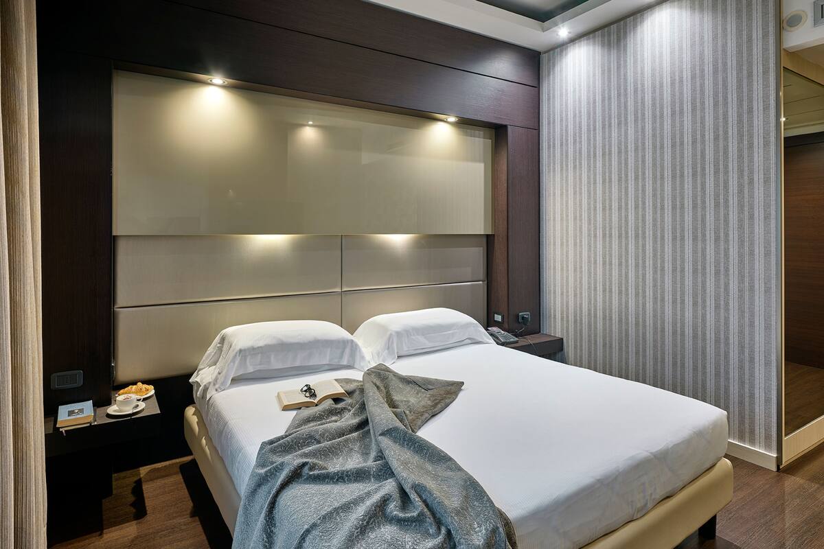 Ein modernes Hotelzimmer mit einem großen Bett, Nachttischen und einem großen Fenster mit Vorhängen.