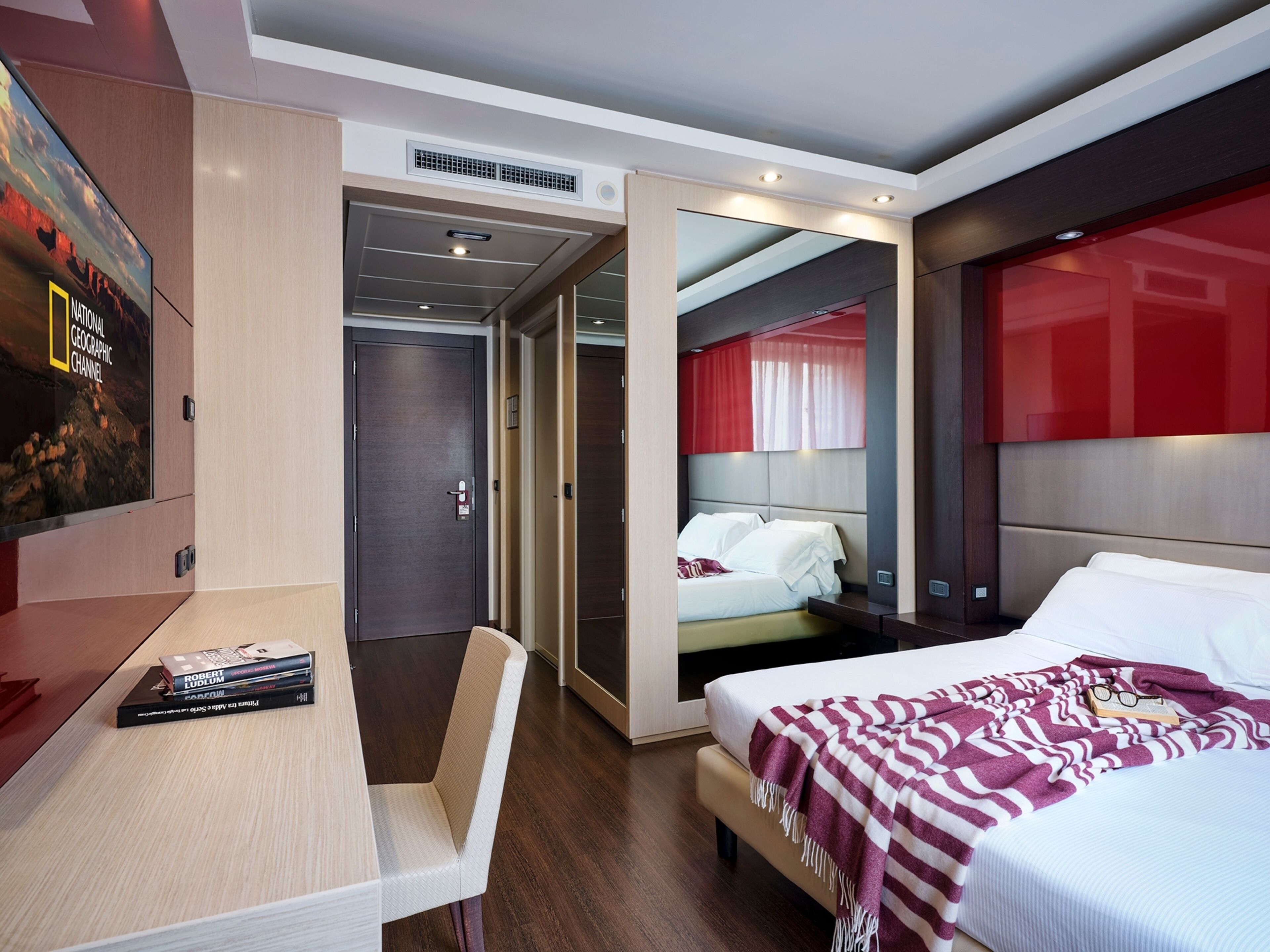 A hotel room with a bed, bedside table, chair, and a TV mounted on the wall.