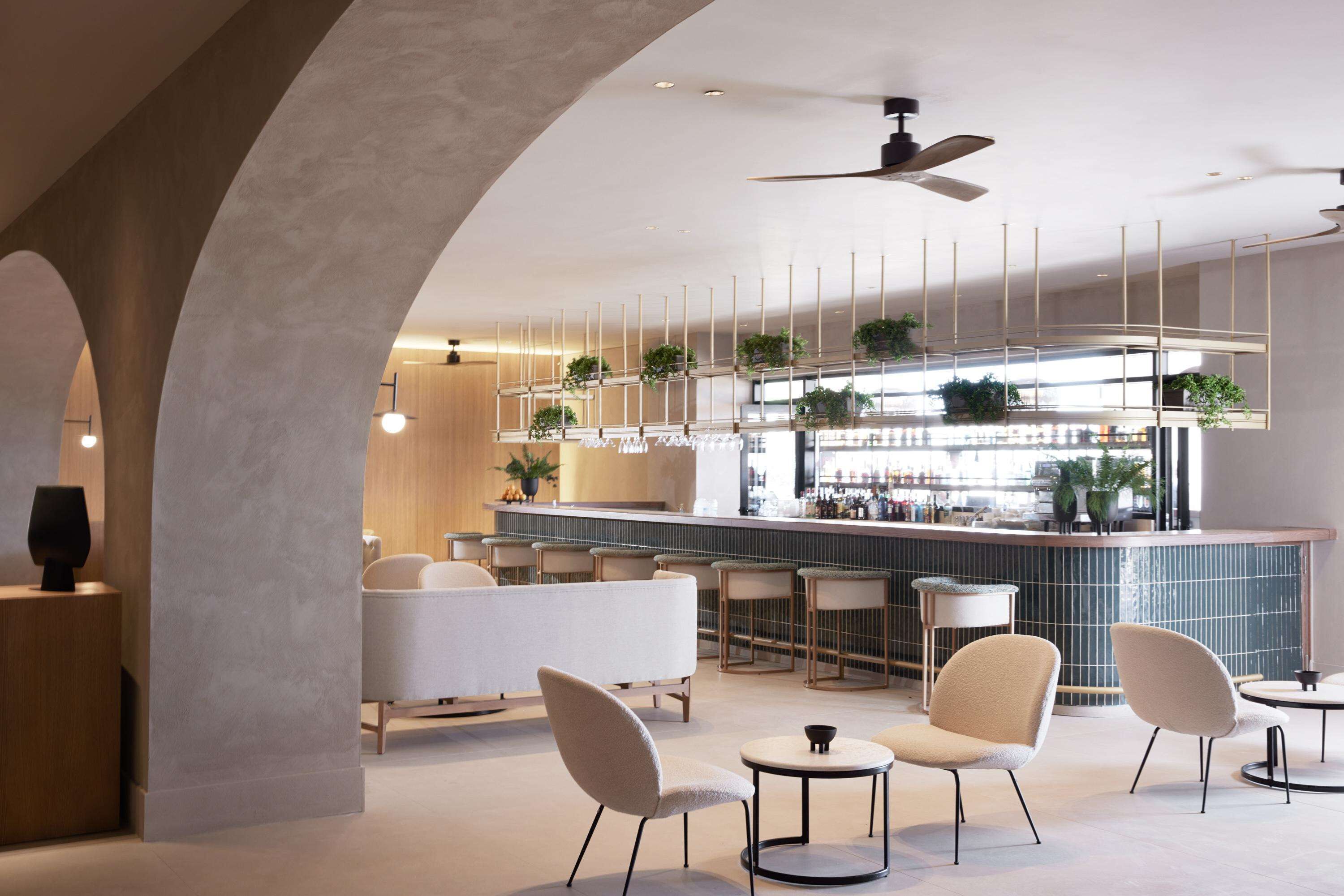 Un moderno bar con barra, asientos y plantas colgantes.