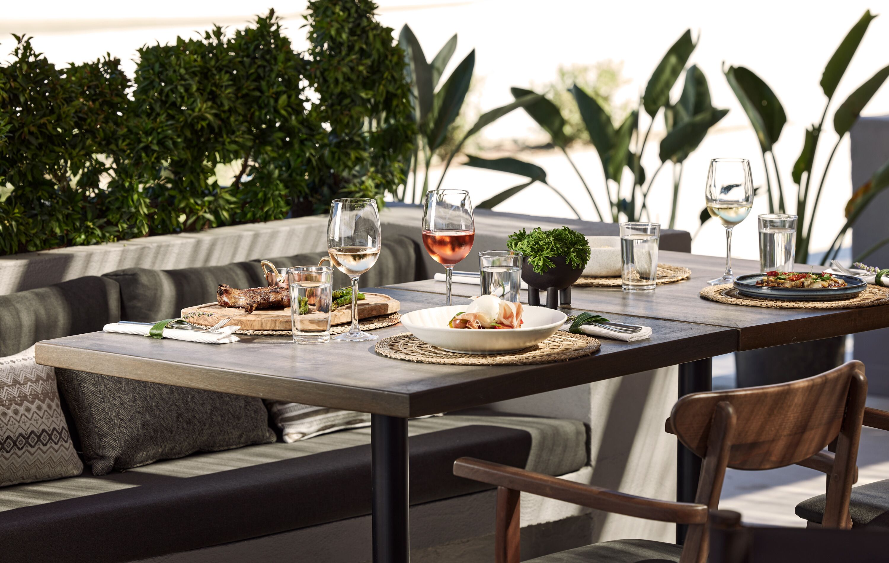 An outdoor dining area with a table set for two, featuring a variety of dishes and glasses of wine.