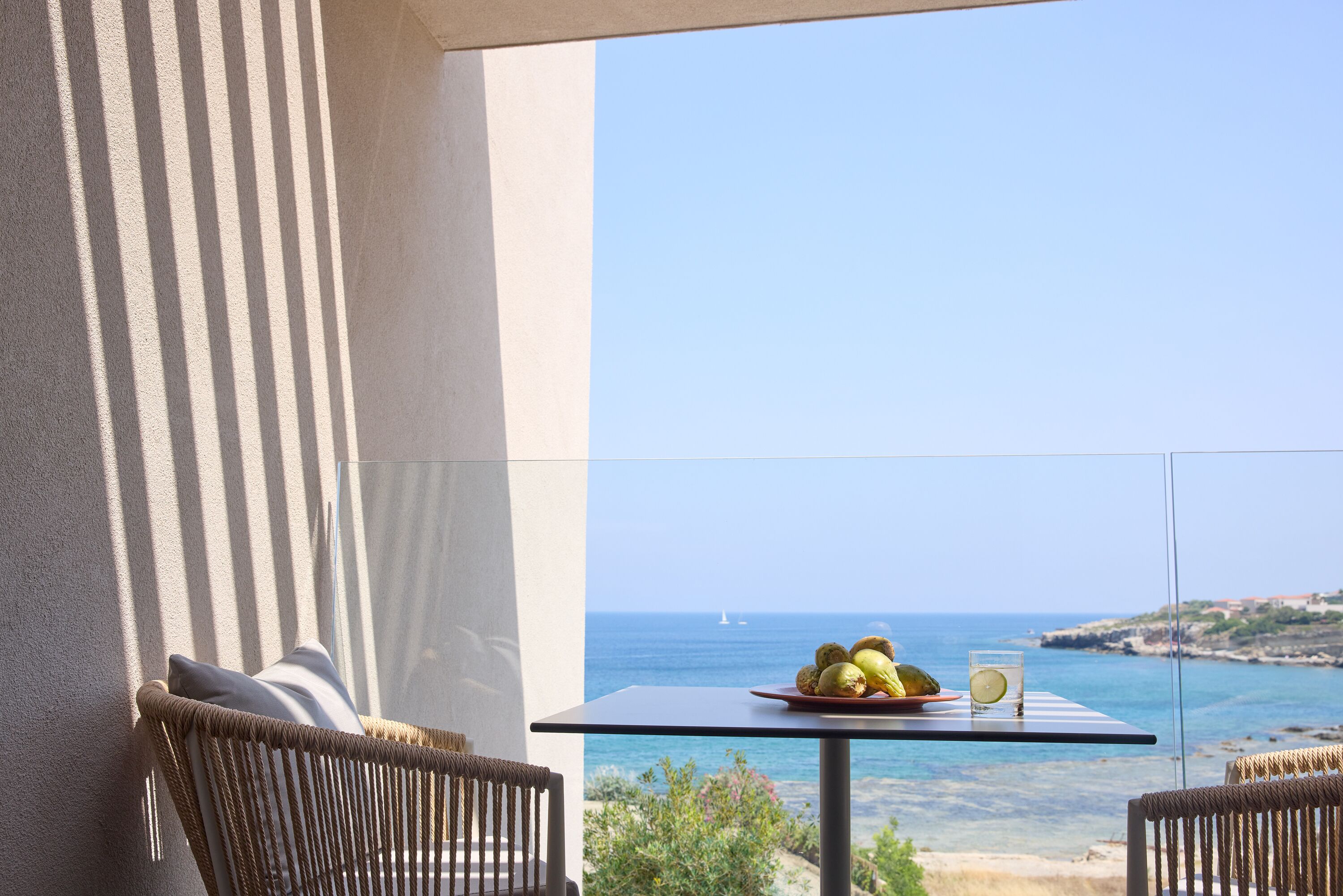 A balcony with wicker furniture, a table with a fruit plate and a glass, and a view of the sea.