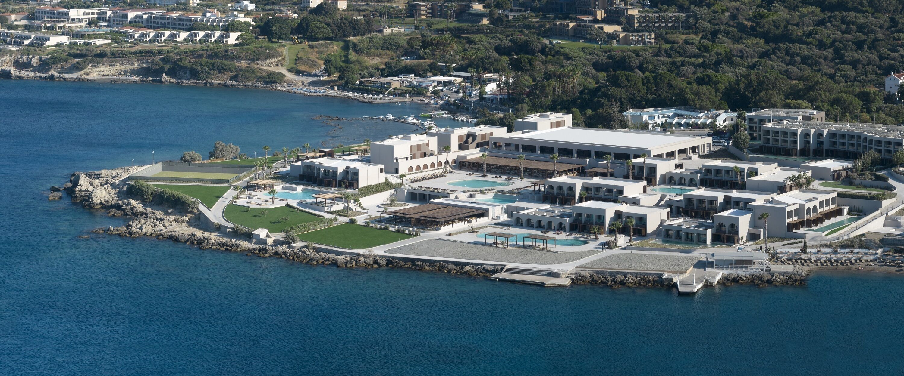 Luftaufnahme eines Küstenhotels mit mehreren Gebäuden, einem großen Pool und einer felsigen Küstenlinie.
