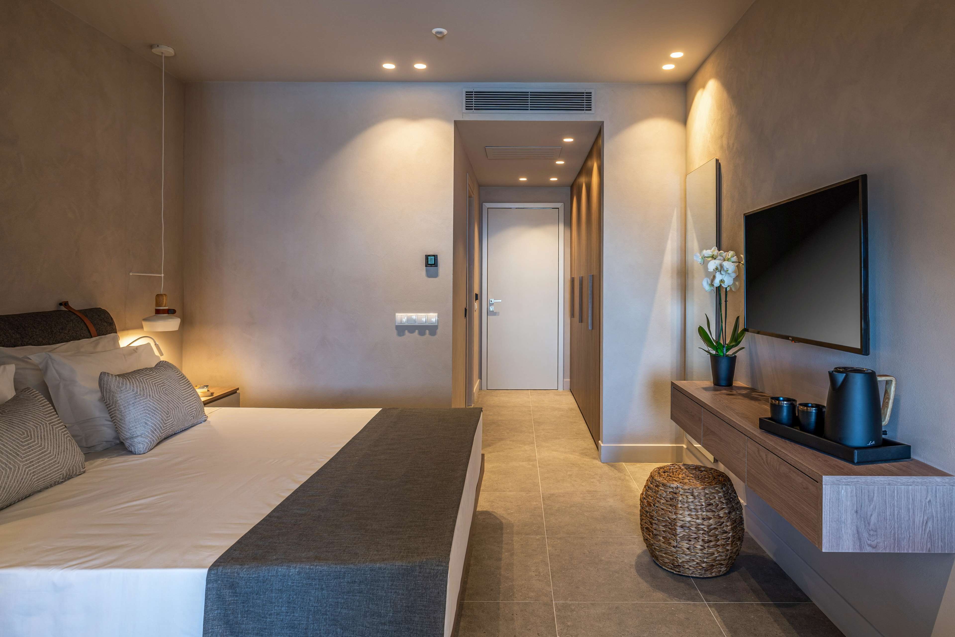 Una habitación de hotel moderna con una cama grande, mesita de noche y televisor montado.