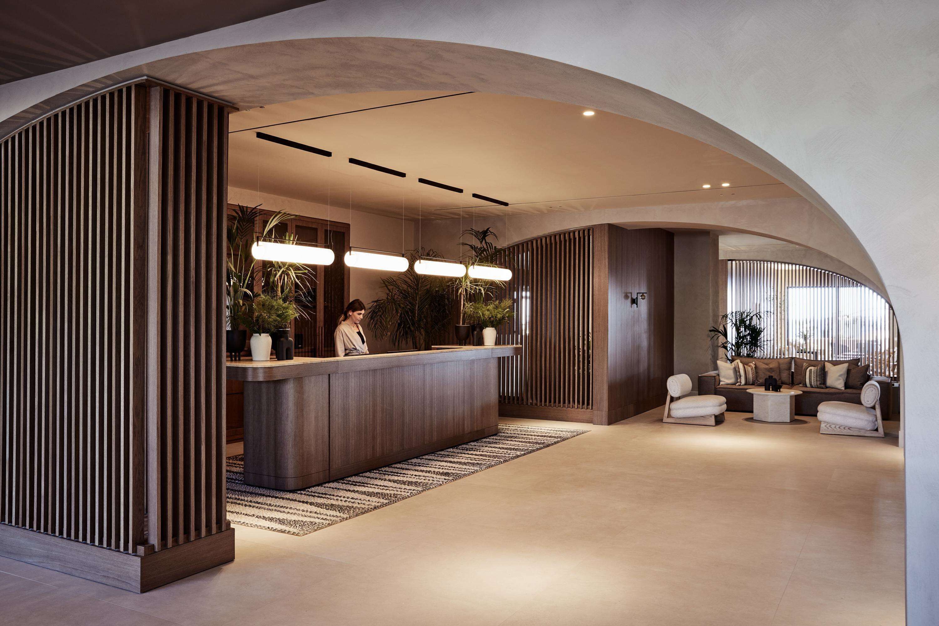Een modern receptiegebied met een gebogen plafond, een receptiebalie, een zithoek en potplanten.