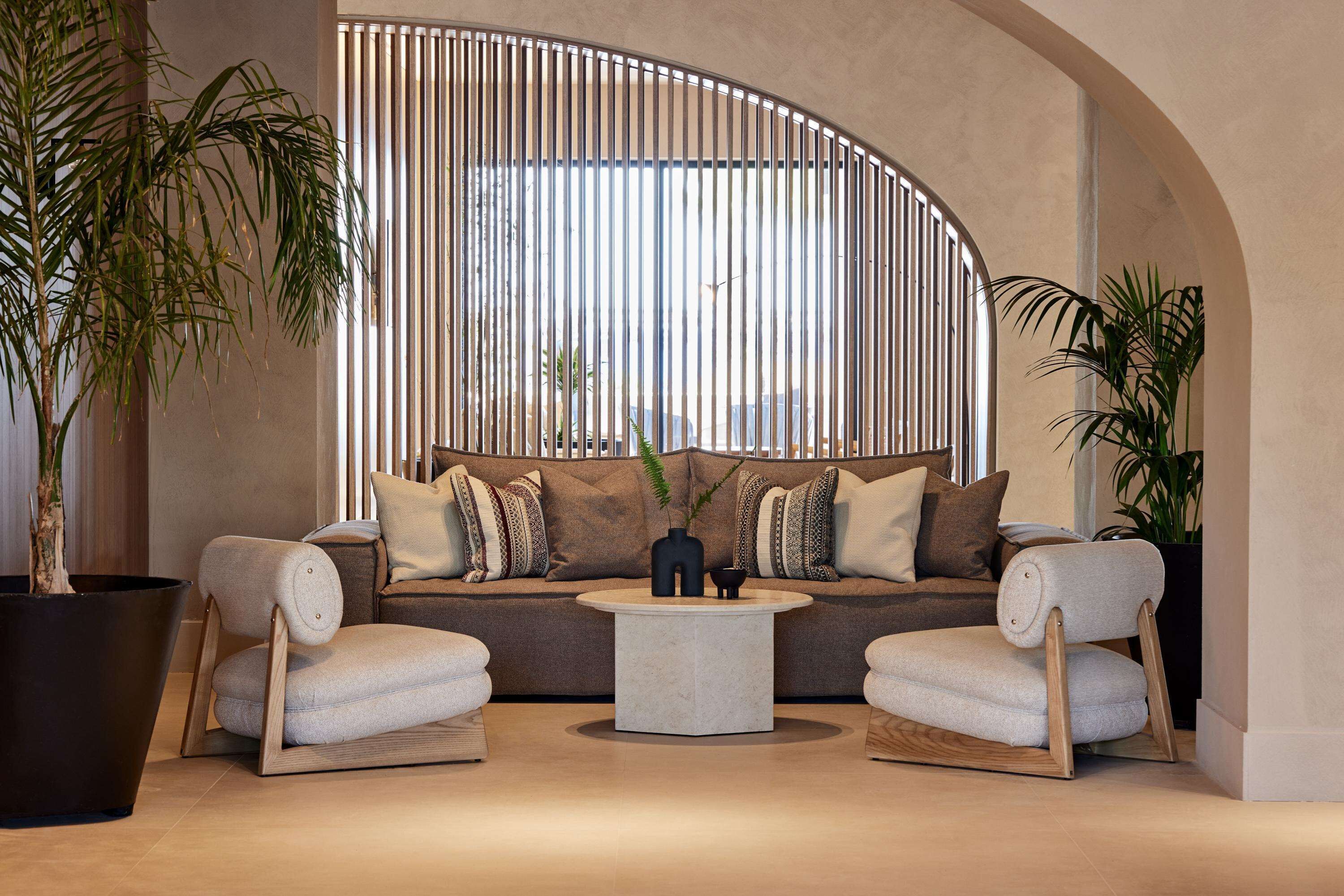 A modern living room with a curved ceiling, a sofa set, two armchairs, a round coffee table, and large potted plants.