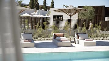 A poolside area with lounge chairs and umbrellas, a wooden fence, and a modern building in the background.