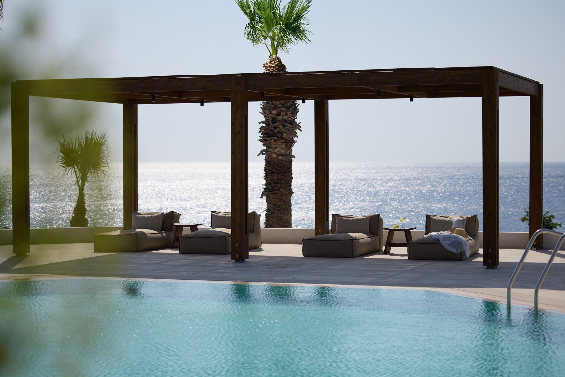 Ein Poolbereich mit einer Holzpergola, Liegestühlen und einer Palme.