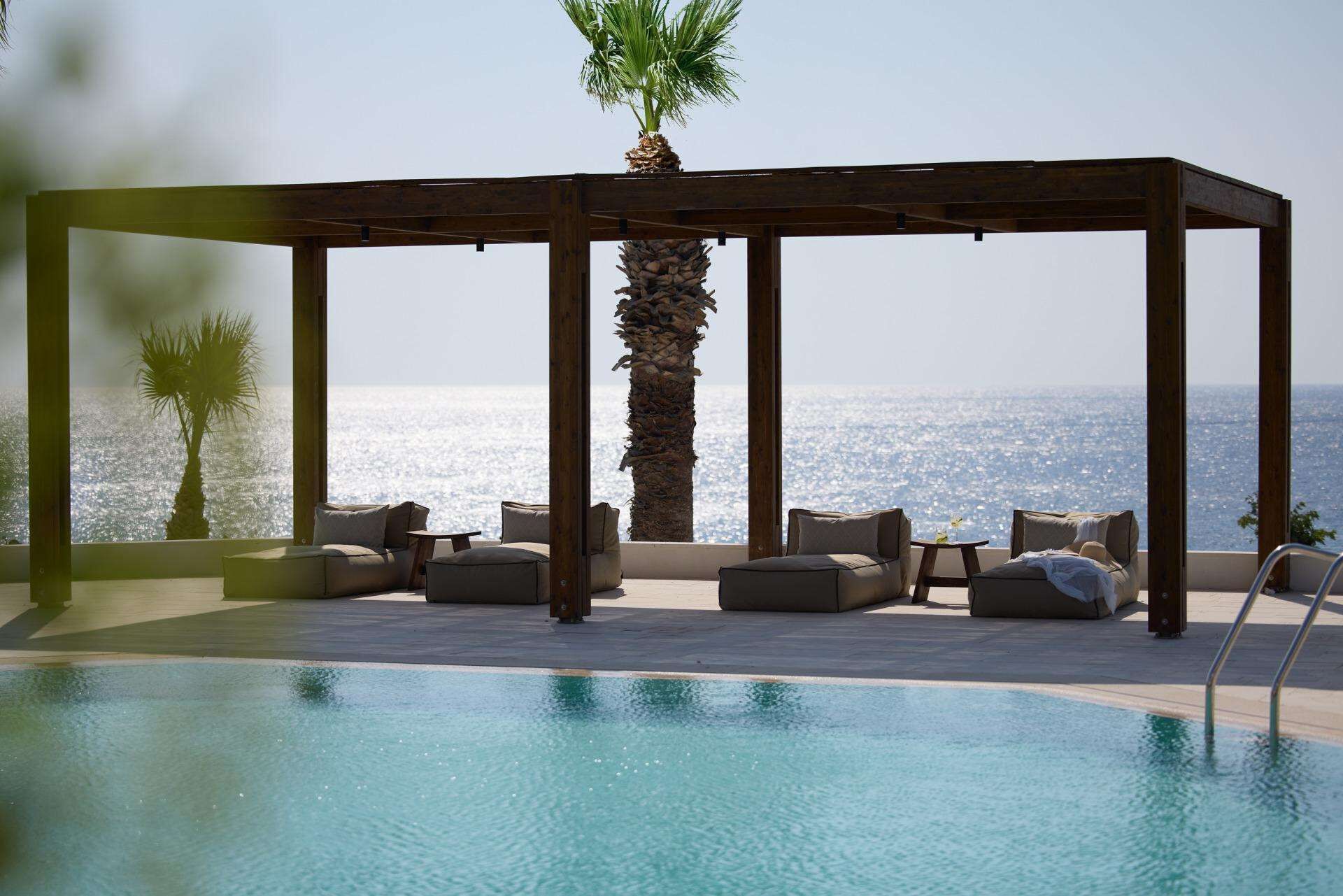 Un espace aménagé au bord de la piscine, avec une pergola en bois, des chaises longues et un palmier.