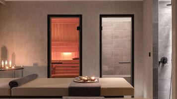 Une salle de spa équipée de deux tables de massage, d’une porte en bois donnant accès à un sauna et d’un espace de douche carrelé.
