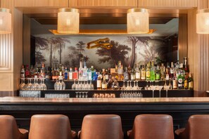 A bar area with a wooden backdrop, a variety of liquor bottles, and multiple glasses. - NH Lyon Airport (Colombier-Saugnieu)