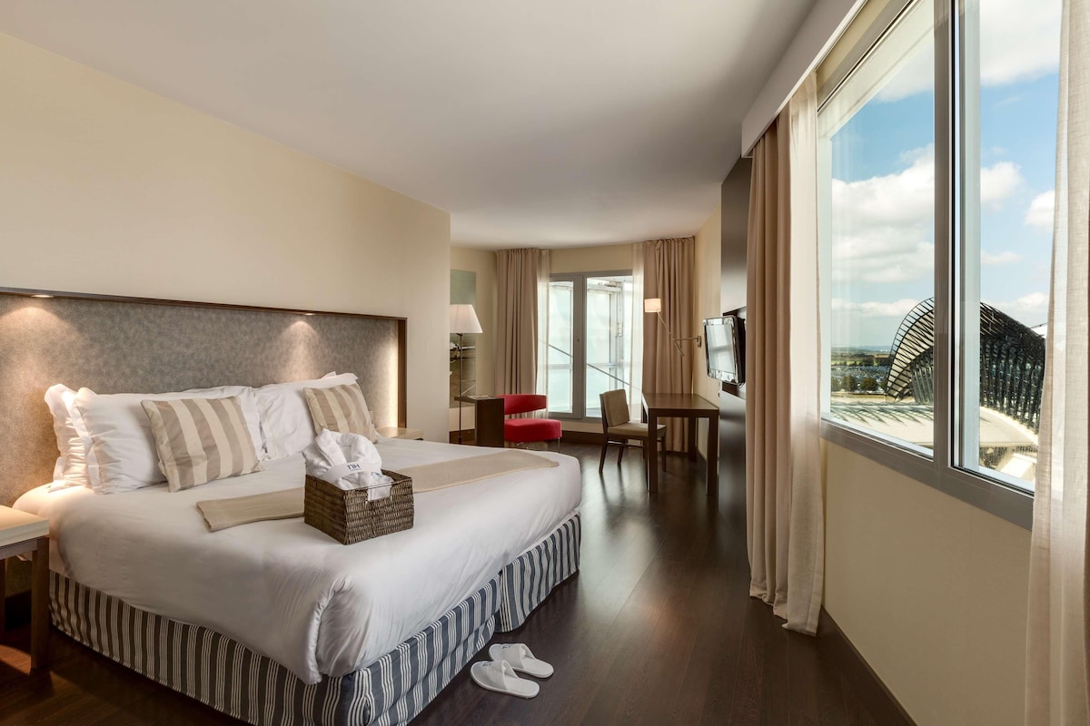A hotel room with a large bed, a desk, a chair, and a TV.