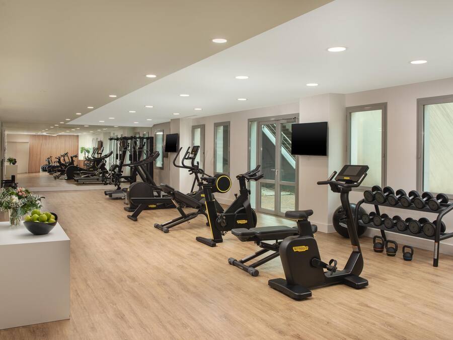 A gym with various exercise machines, a wall-mounted TV, and a rack of dumbbells.