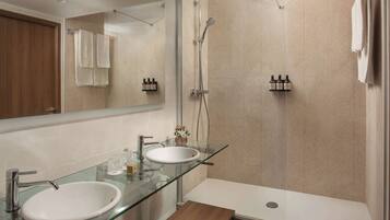 A modern bathroom with two sinks, a glass countertop, a shower, and a wooden bench.