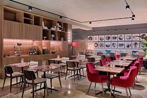 A modern restaurant with wooden shelves, tables, and red chairs. - NH Lyon Airport (Colombier-Saugnieu)