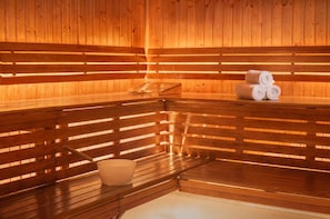 A sauna with wooden benches, a bench with a towel and a bowl, and towels stacked on the bench.