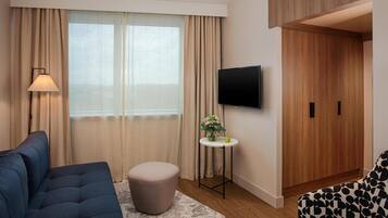 Ein modernes Hotelzimmer mit einer Couch, Hocker, Fernseher und einem Holzschrank.