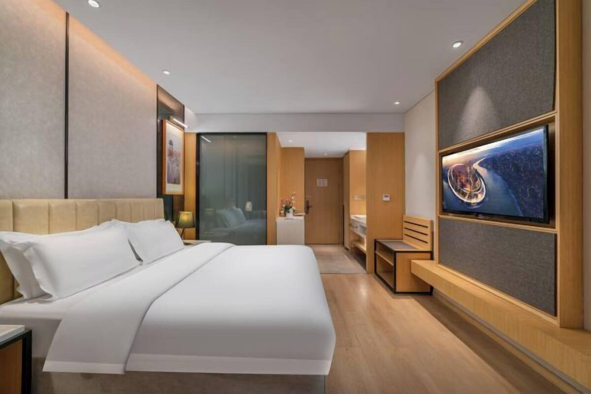 A modern hotel room with a large bed, a TV mounted on the wall, and a small seating area.