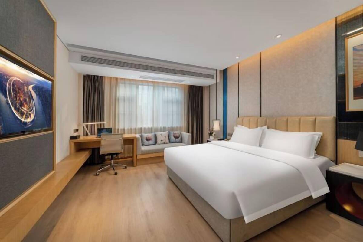 A modern hotel room with a large bed, a desk, and a seating area.