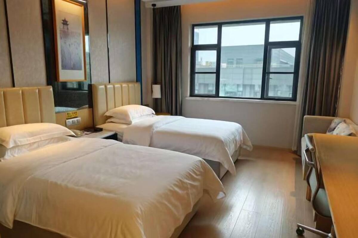 A hotel room with two beds, a bedside table, a chair, and a window with curtains.