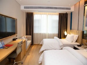Habitación de hotel con dos camas, un escritorio con silla, televisor y un ventanal con cortinas.