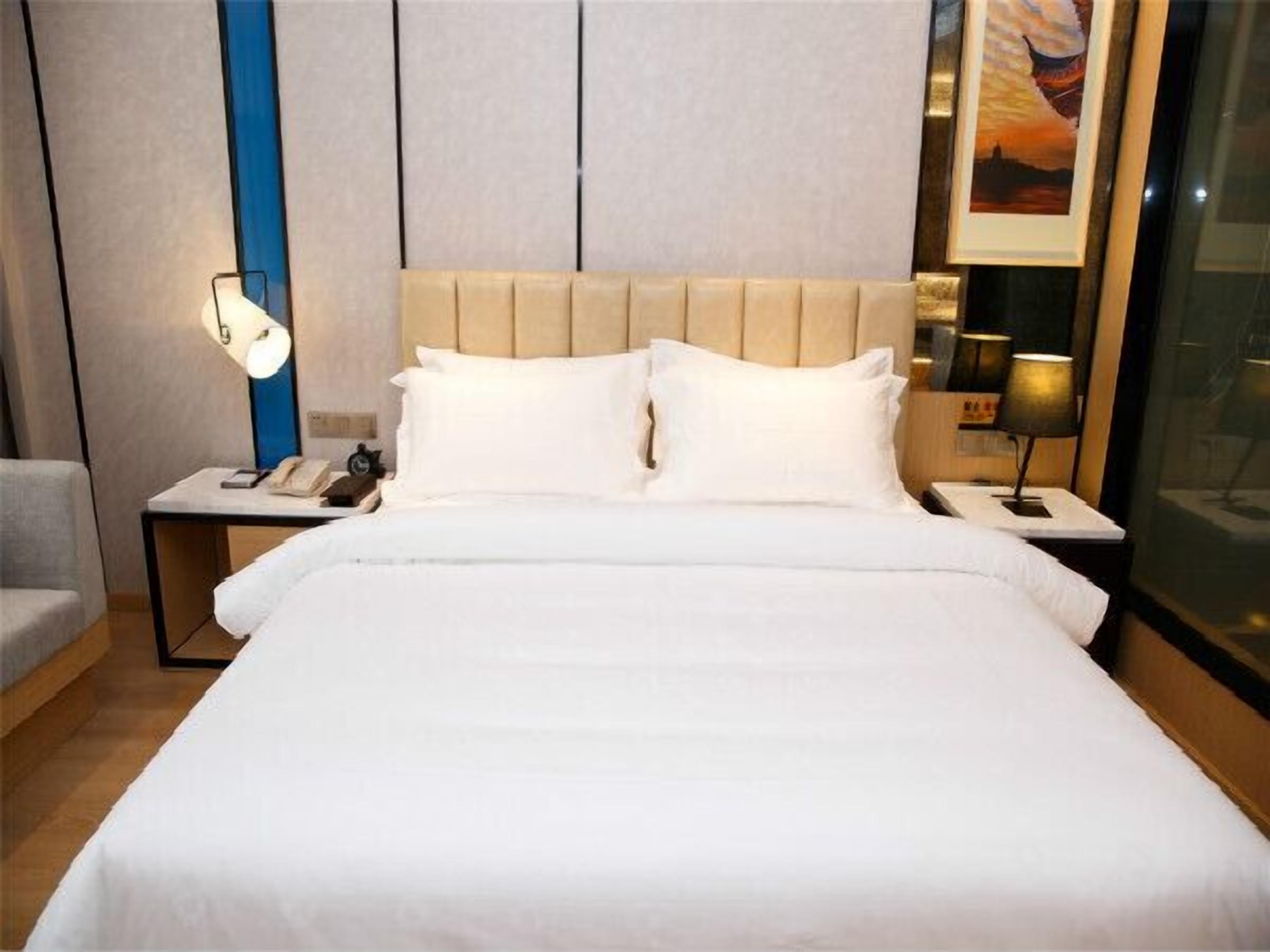 Ein Hotelzimmer mit einem großen Bett, zwei Nachttischen, einer Wandlampe und einem Bild an der Wand.