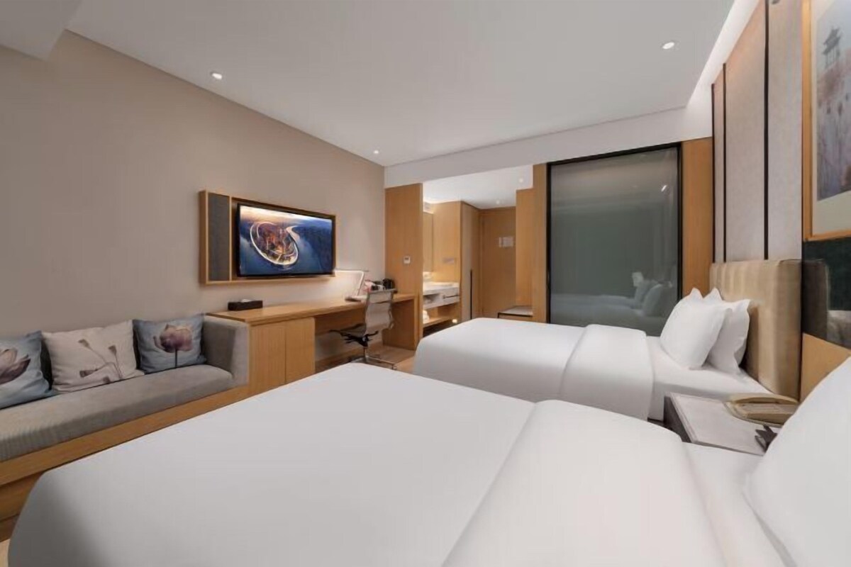 A modern hotel room with a large bed, a desk, a sofa, and a painting on the wall.