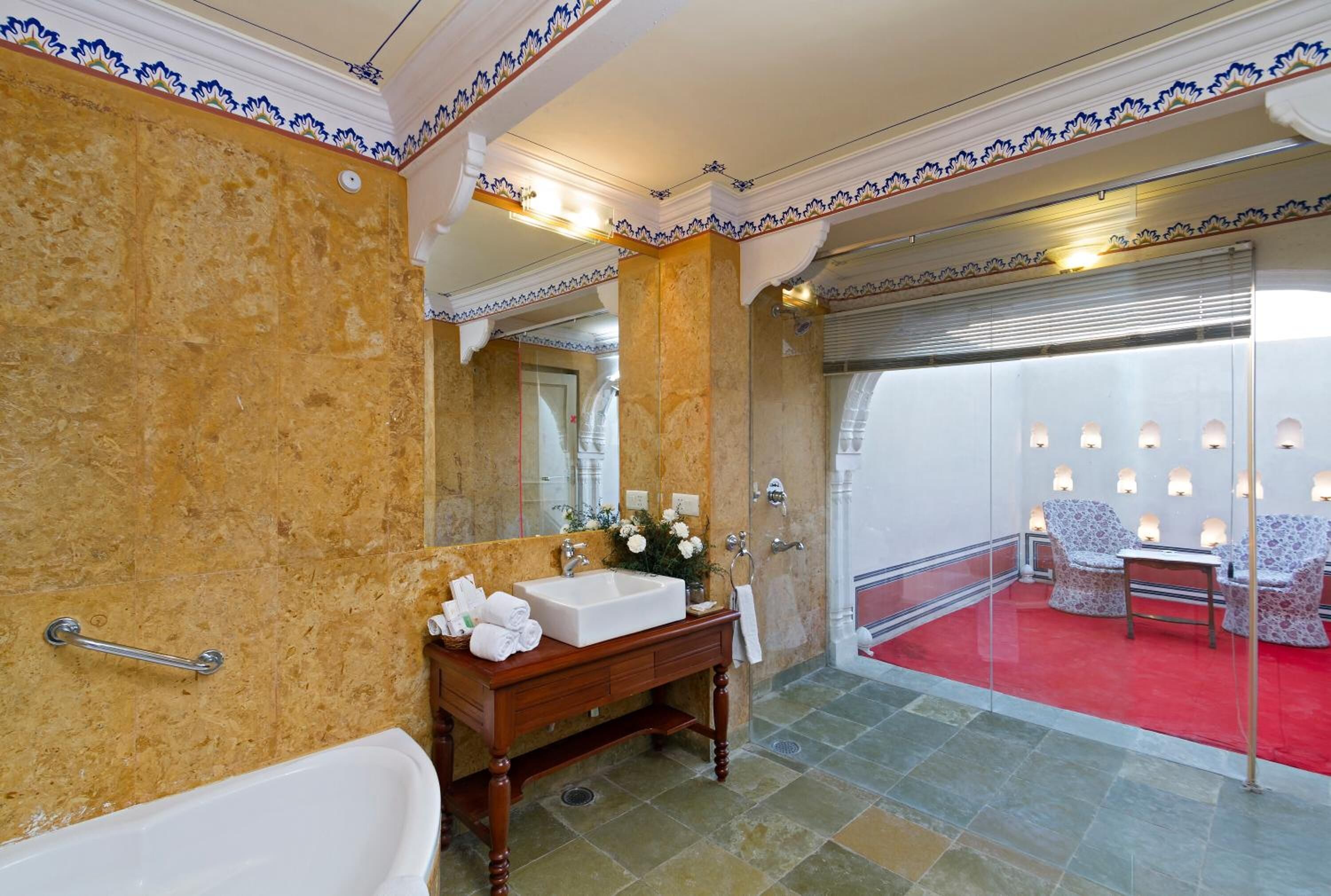 A bathroom with a marble wall, a wooden vanity, a white bathtub, and a red carpeted area with seating.