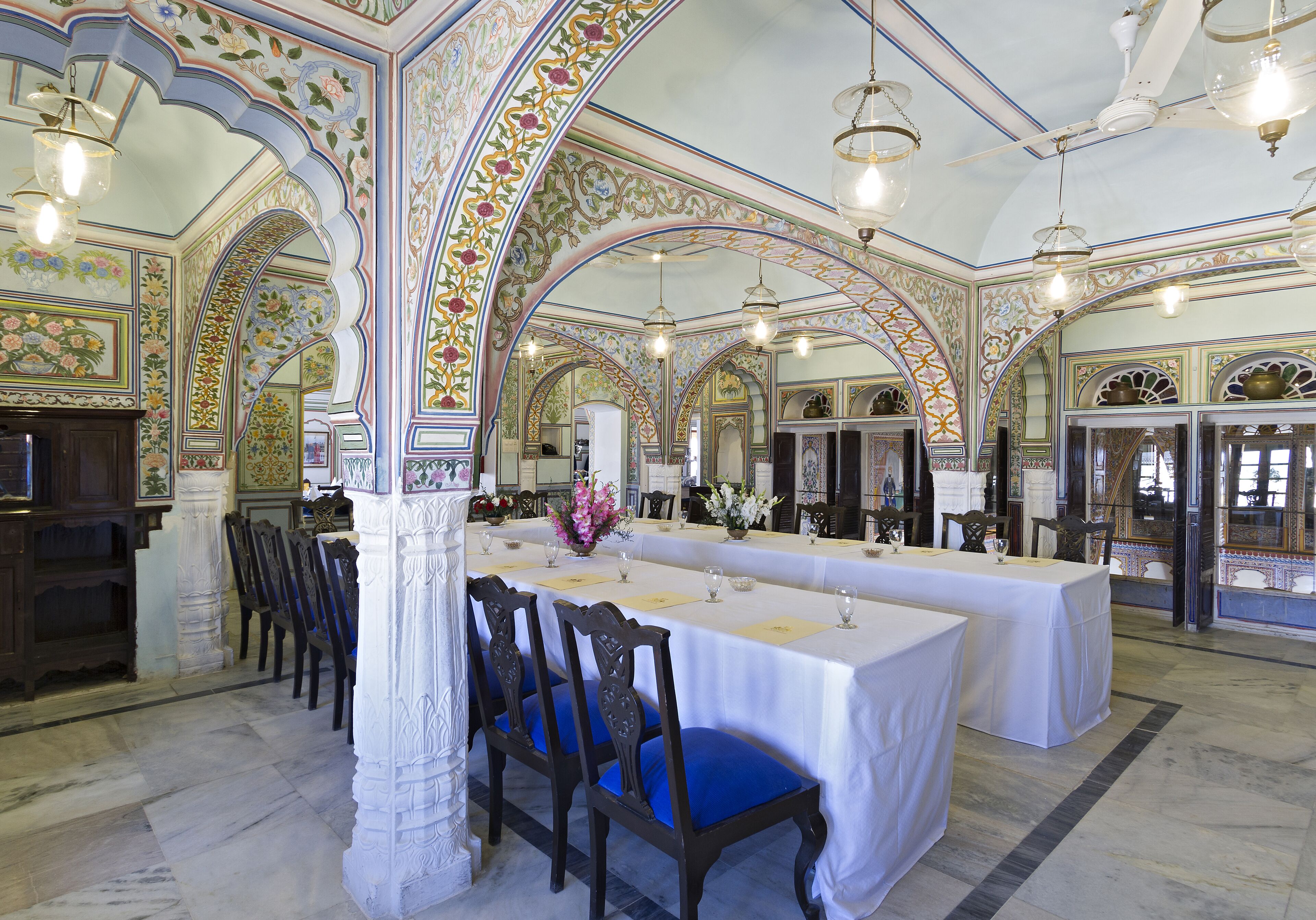 Un comedor con arcos decorativos, una mesa larga dispuesta para una comida y sillas tradicionales.