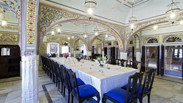 Une longue table à manger, des chaises bleues, un plafond décoré et des lustres.
