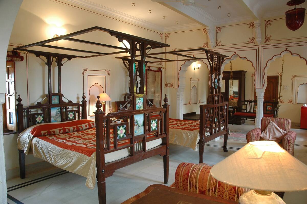 Una habitación tradicional con una cama con dosel, una zona de estar con una silla y una lámpara.