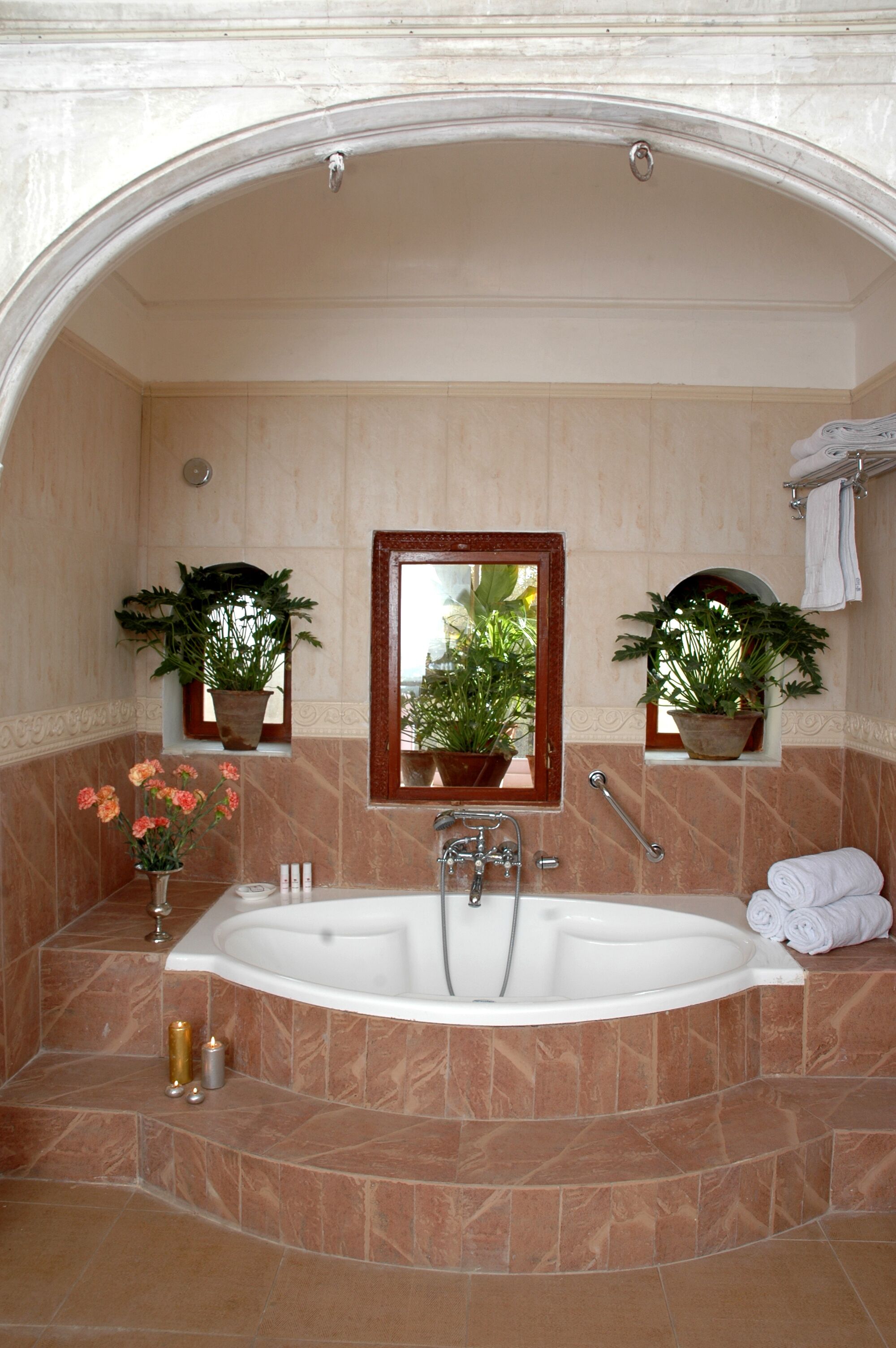 Un baño con una bañera grande, dos plantas en macetas, un espejo y un perchero para toallas.