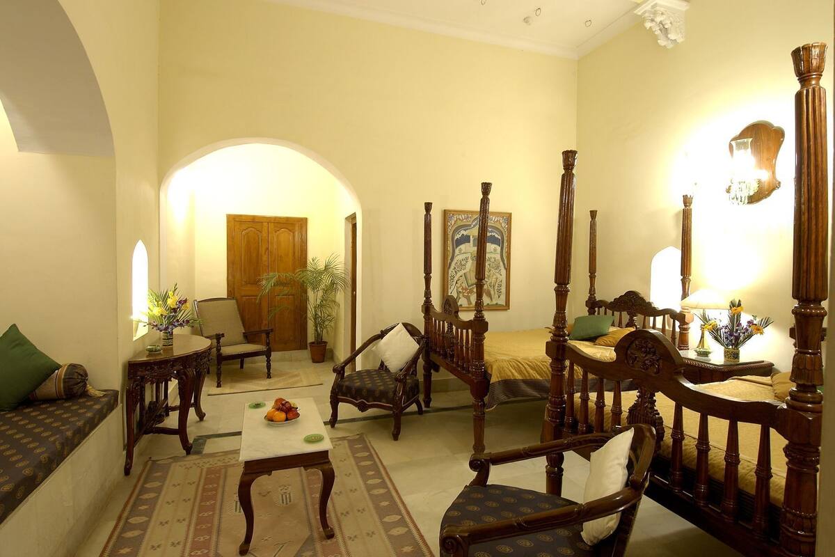 Habitación tradicional con cama con dosel, un sofá, una silla, una mesa y una puerta.