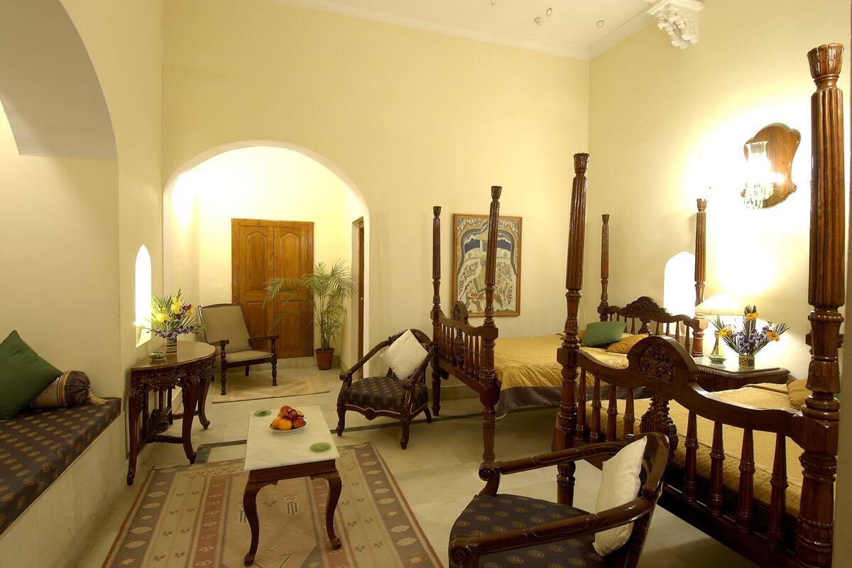 Habitación tradicional con cama con dosel, sofá, sillón y pequeña mesa con frutero.