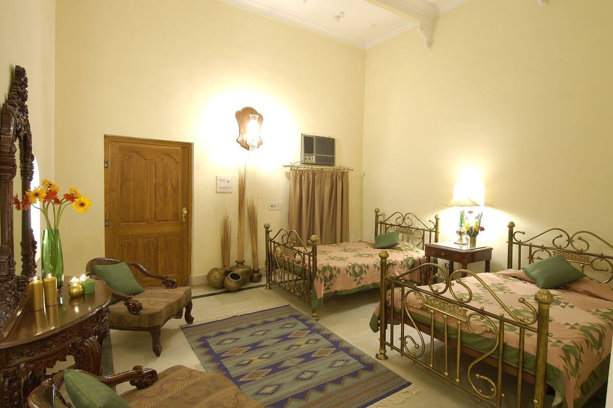 Una habitación con dos camas, una puerta de madera, un espejo, un jarrón con flores y una mesa con velas.